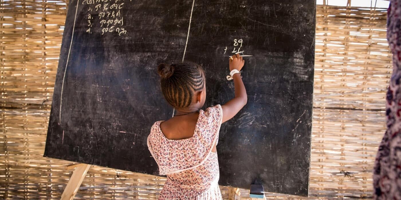 A child writing on a chalkboard at the school built by NRC in Um Rakuba camp.
